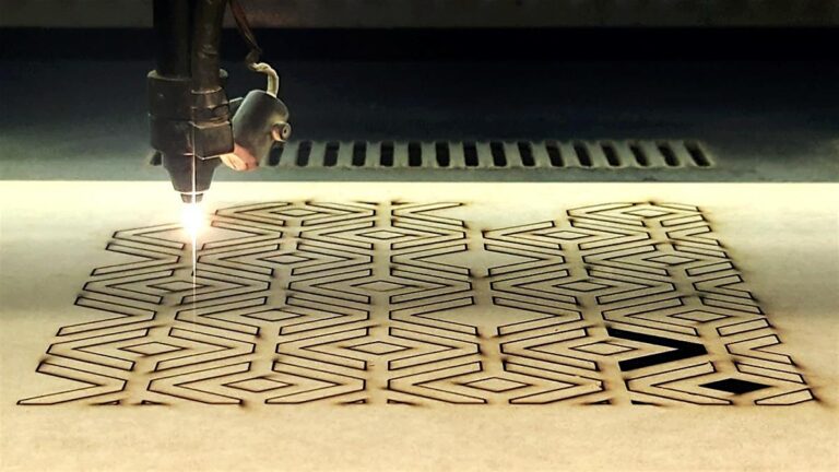 Close-up of a 100W CO2 laser cutter at Maker Cube cutting zig-zag slots into an MDF sheet; laser head in motion and kerf line visible (Langley, BC)