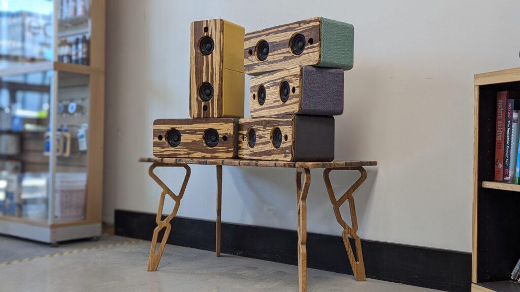 Handmade wooden Bluetooth speakers stacked on the Maker Cube reception table in Langley, BC, colorful fabric wrapped sides and a striped European beech front