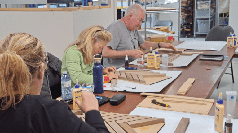 Participants at Maker Cube gluing black walnut strips to an MDF backer in a herringbone pattern, leaving gaps for epoxy to pour between, Epoxy Charcuterie workshop, Langley, BC