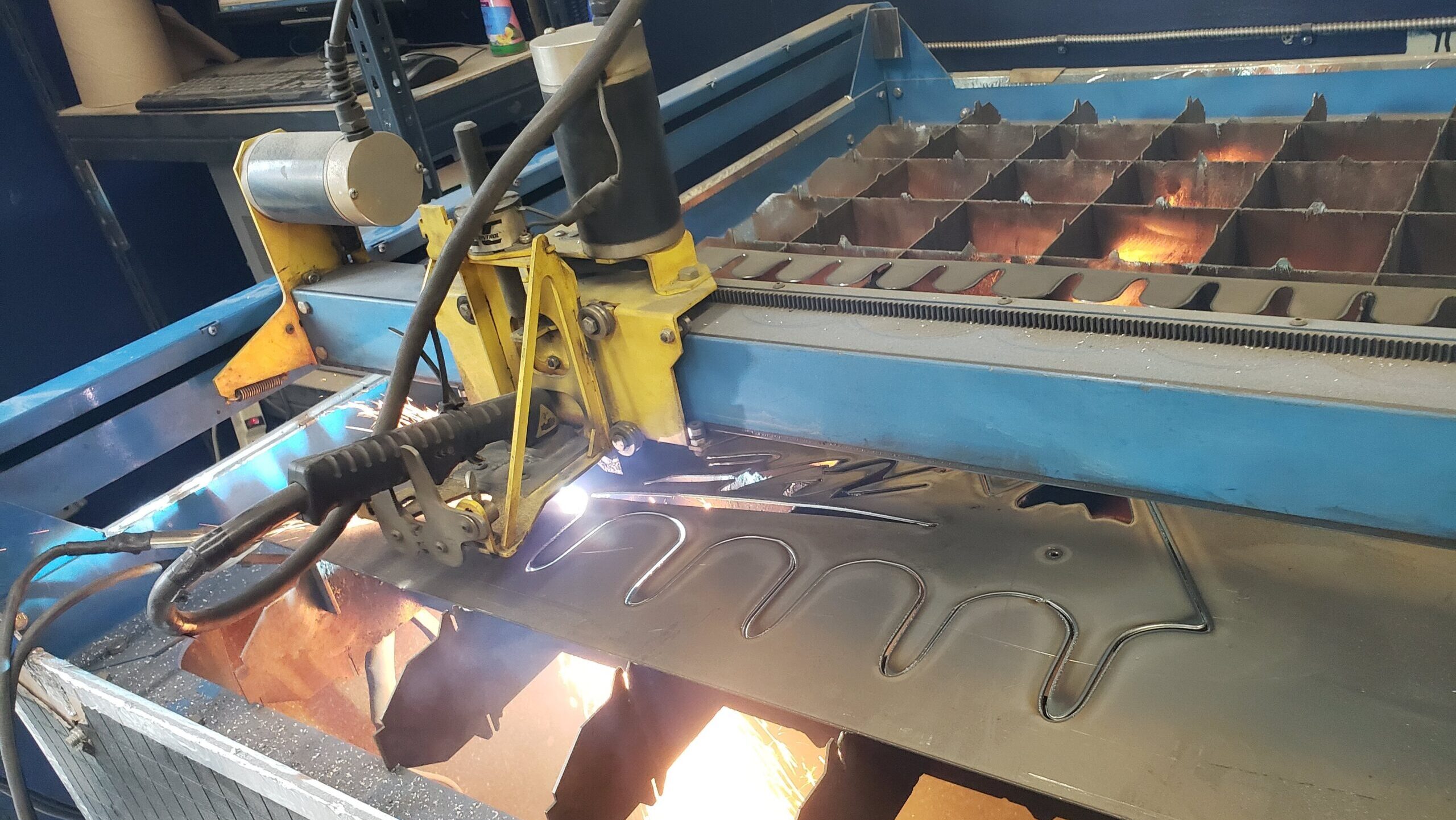 CNC plasma table at Maker Cube cutting a steel sheet, sparks under the plate and a glowing torch above, a large coat hanger with hooks being cut by Monty, 4x4 table rated for up to 3/8" steel, Langley, BC