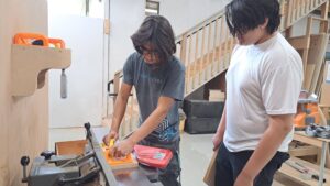 Two participants at Maker Cube in Langley, BC, one in a Maker Cube uniform demonstrating the 8 inch industrial jointer while milling a board with yellow push blocks