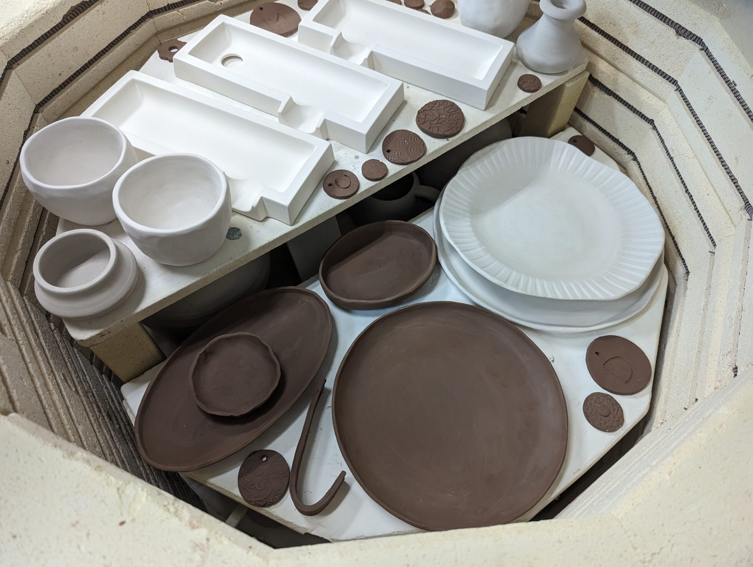 Inside the kiln at Maker Cube in Langley, BC, multiple shelves loaded with pottery pieces ready for bisque and glaze firing