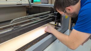 Participant at Maker Cube in Langley, BC, wearing safety glasses and adjusting the focus height of a 100W CO2 laser cutter head for a crisp cut
