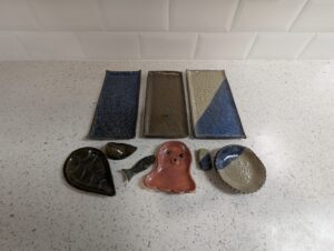Three handmade sushi platter sets from Maker Cube’s handbuilding pottery class in Langley, BC, each with different glazes and styles, including a floral set with a leaf shaped sauce dish and leaf shaped chopstick rest, and an animal set with an octopus sauce dish and fish shaped chopstick holder