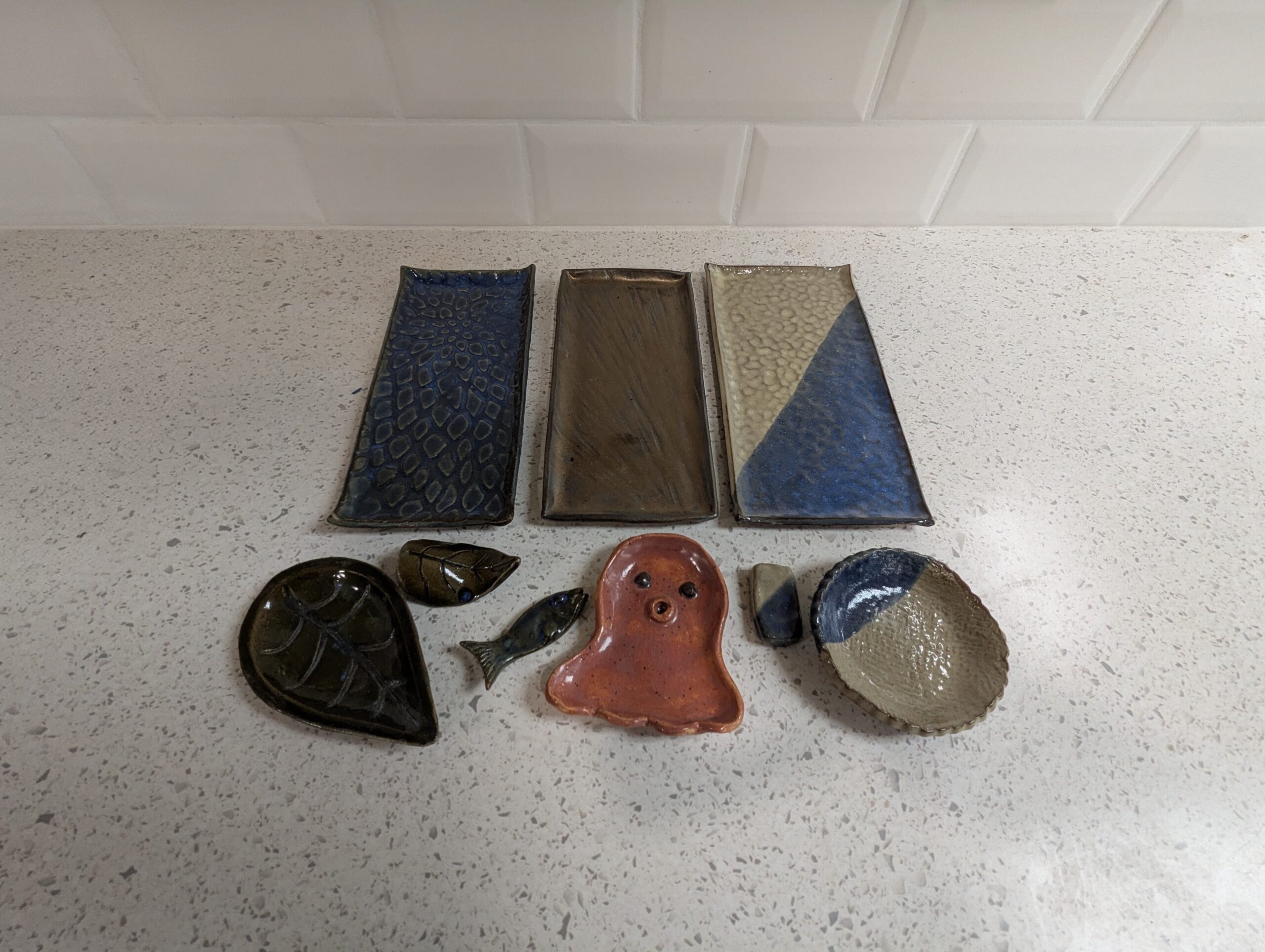 Three handmade sushi platter sets from Maker Cube’s handbuilding pottery class in Langley, BC, each with different glazes and styles, including a floral set with a leaf shaped sauce dish and leaf shaped chopstick rest, and an animal set with an octopus sauce dish and fish shaped chopstick holder