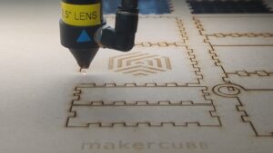 Close up of a 100W CO2 laser cutter at Maker Cube in Langley, BC, engraving the Maker Cube logo and cutting parts for a project box from MDF