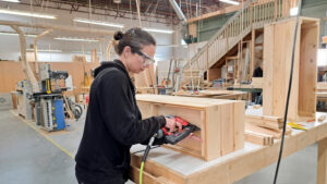 Participant using a nail gun to assemble a cedar planter box in a woodworking class at Maker Cube Langley BC