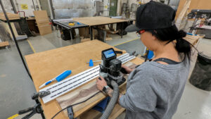 Woman using Shaper Origin handheld CNC to engrave a large wood slab in a woodworking shop in Langley BC