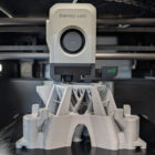 Bambu Lab 3D printer at Maker Cube in Langley, BC, printing a complex structural component for a microscope with visible layered filament