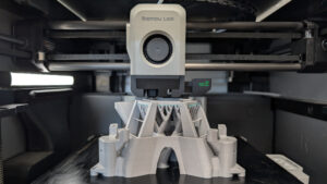 Bambu Lab 3D printer at Maker Cube in Langley, BC, printing a complex structural component for a microscope with visible layered filament